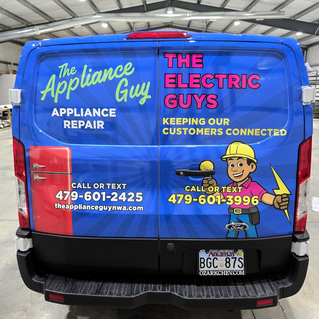 The Appliance Guy The back of a blue service van with logos for The Appliance Guy and The Electric Guys, phone numbers, and cartoon images of a man with tools and another man in a hard hat holding a lightning bolt.