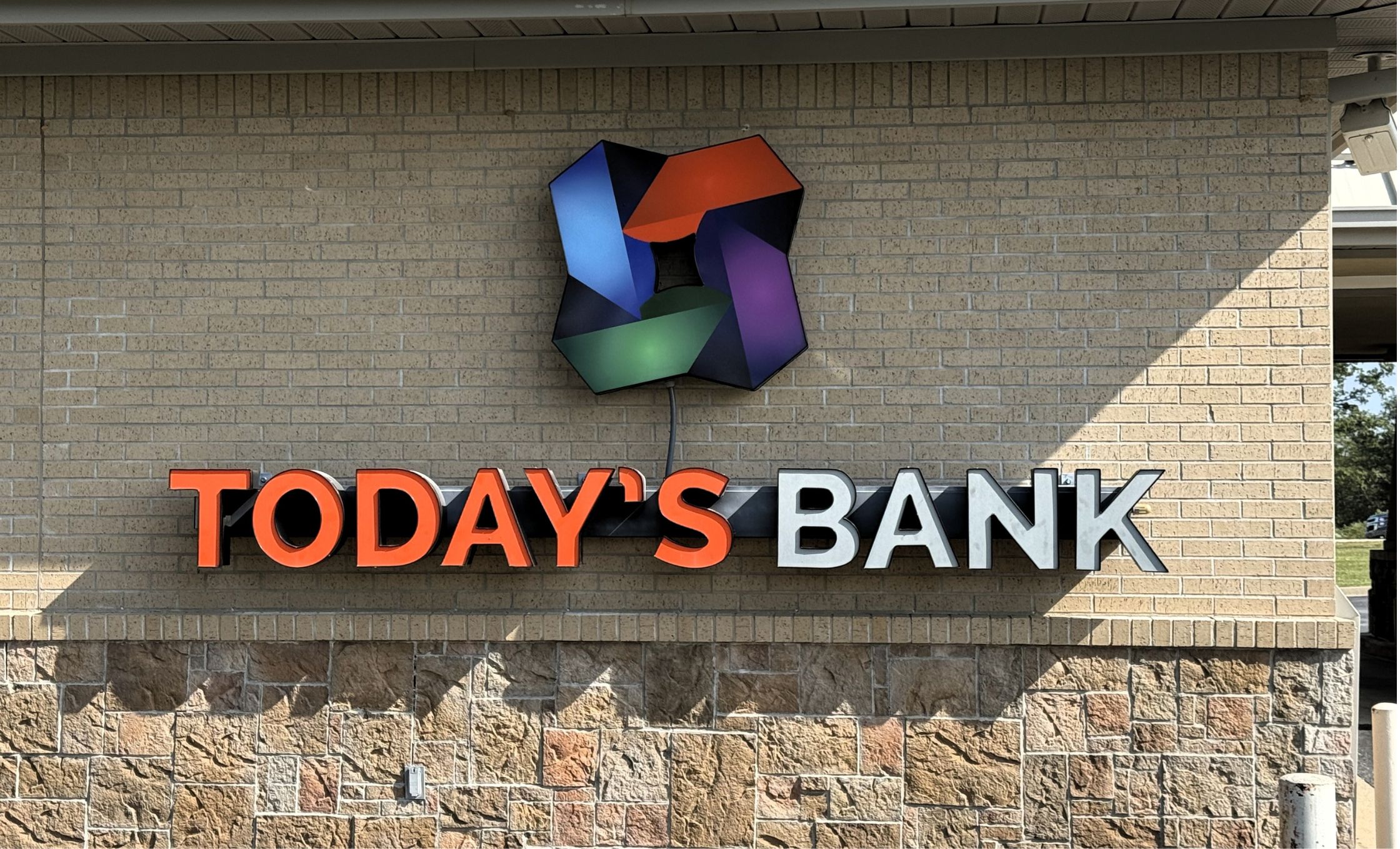 A modern building with a sign reading Vold Vision: Your Sight Is Our Vision above the entrance. A parked service truck with a ladder is on the right. Green grass and a large tree are visible, under a clear blue sky.