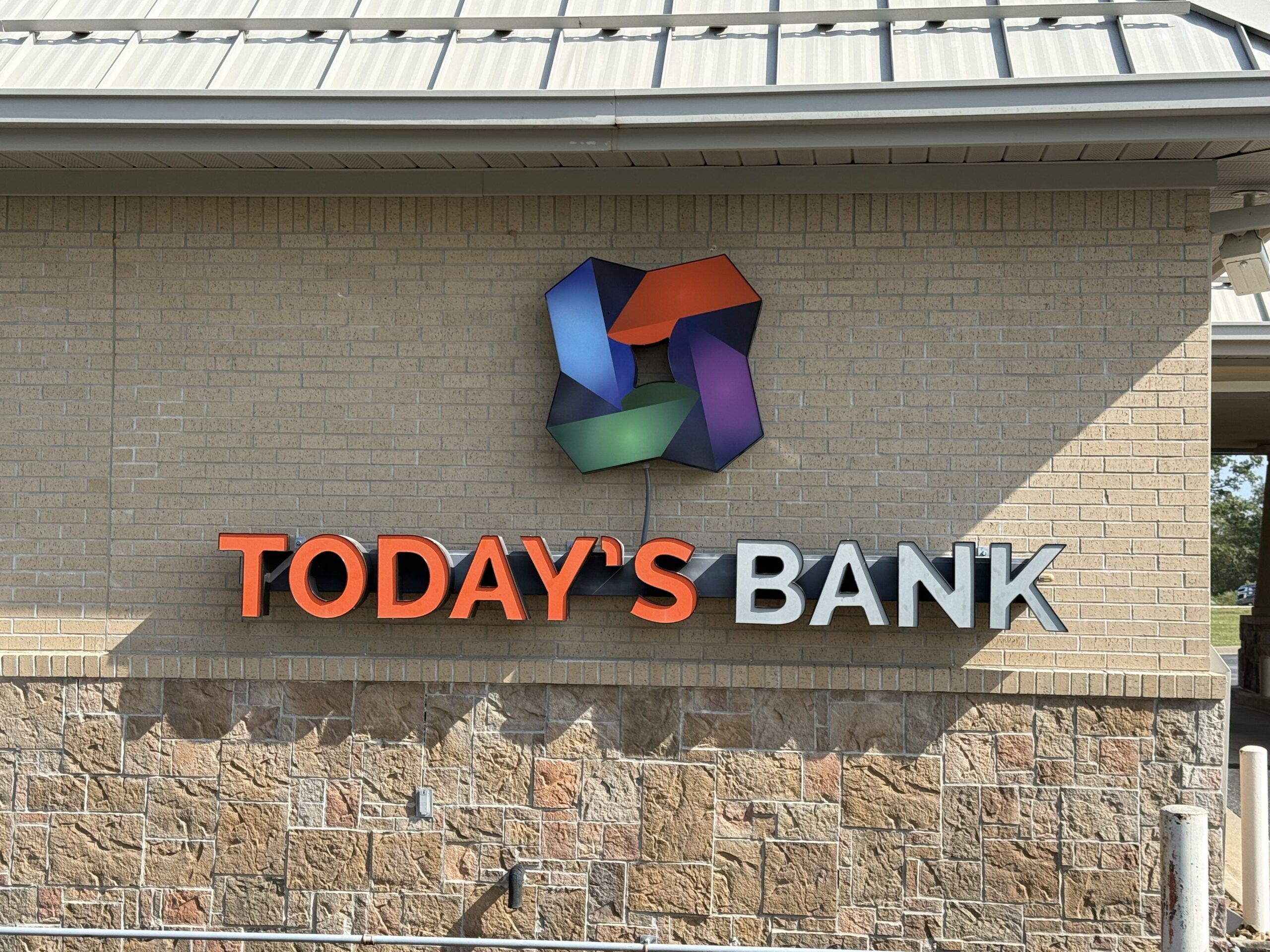 Sign on a brick building reads TODAYS BANK with TODAYS in orange and BANK in silver. Above the text is a colorful geometric logo featuring shades of blue, purple, green, and red.