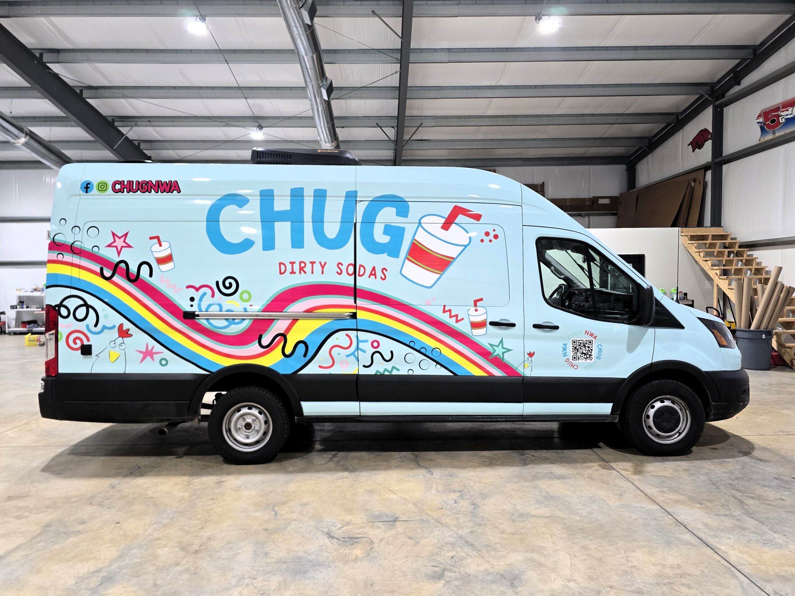A light blue van with colorful rainbow designs, streamers, and soda cup illustrations. The side reads CHUG DIRTY SODAS in large letters. The van is parked inside a spacious, industrial-style building.